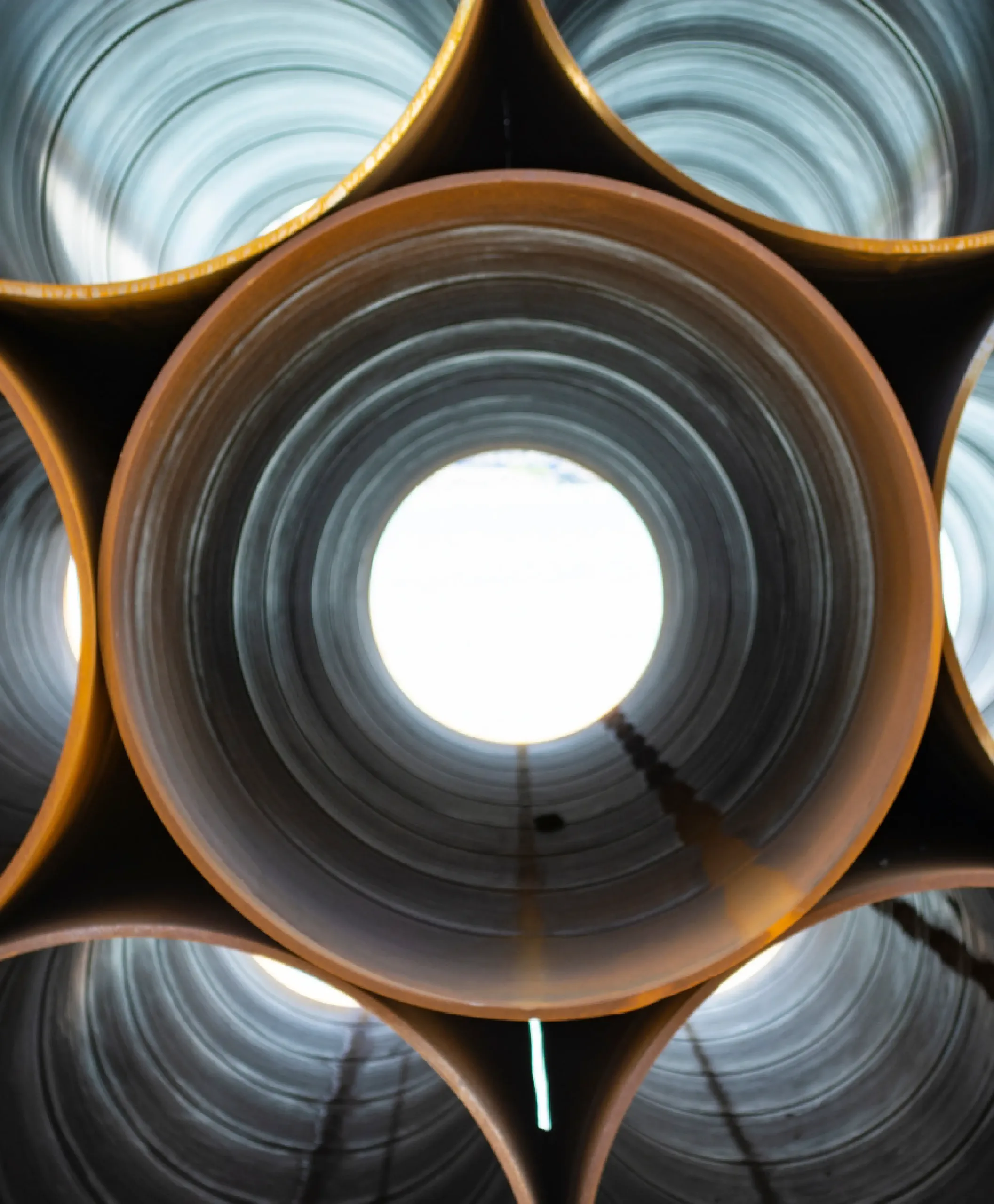 Stacked large metal pipes viewed from one end, showing circular openings and light shining through the centers—ideal materials often used in water line repair projects.