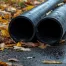 Sewer line pipes on black pavement and fallen golden amber tree leaves.