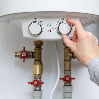 A person adjusts the temperature dial on an electric water heater with visible pipes and control panel, ensuring optimal performance after recent Water Heater Installation & Repair.